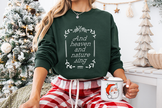 Person wearing a green Christian sweatshirt with text and red plaid pants, holding a mug with Santa Claus design, in a festive setting.