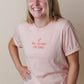 Person wearing a light pink faith based  t-shirt with text, standing against a plain background