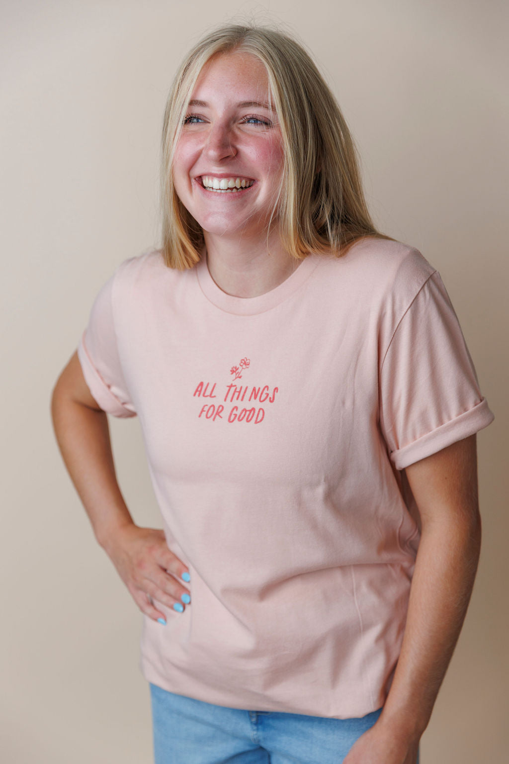 Person wearing a light pink faith based  t-shirt with text, standing against a plain background