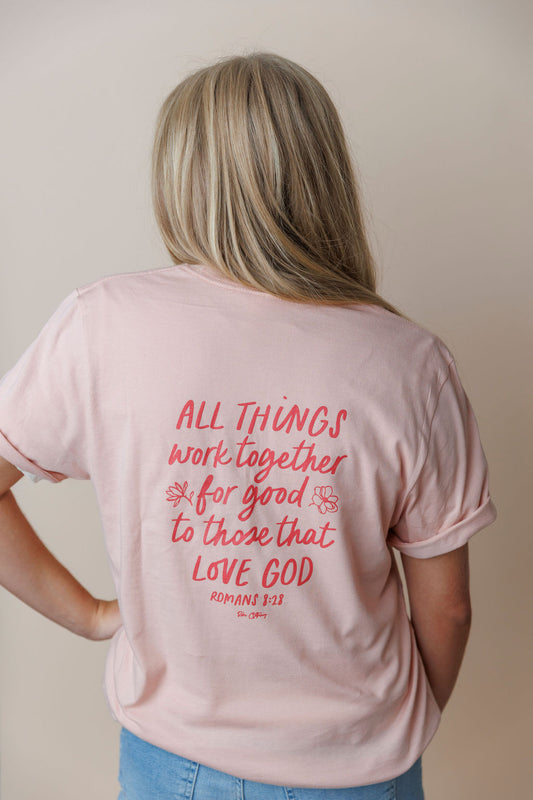 Person wearing a pink t-shirt with a Christian Bible Verse quote on the back against a plain background