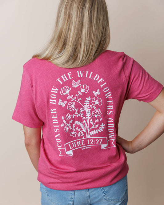 Person wearing a pink t-shirt with a Christian floral design and text on the back, with the phrase CONSIDER HOW THE WILDFLOWERS GROW